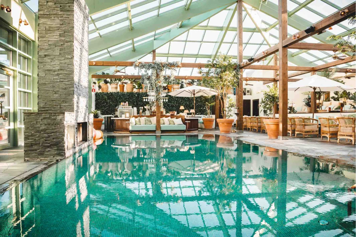 Inomhuspool med turkost vatten under glastak på Falkenberg Strandbad spa med loungemöbler och gröna växter