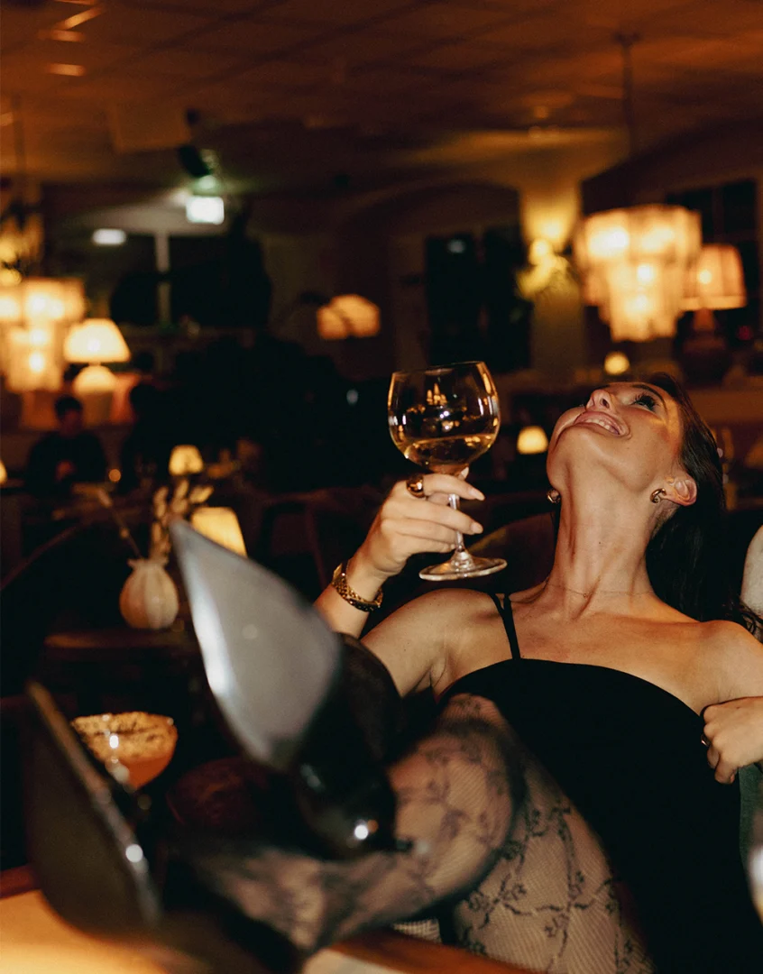 Kvinna njuter av gyllene drink i mysig restaurangmiljö med varmt ljus och elegant inredning