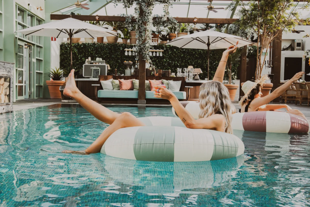 Gäster njuter i poolen med uppblåsbara ringar på Falkenberg Strandbad med poolbar och lounge i bakgrunden