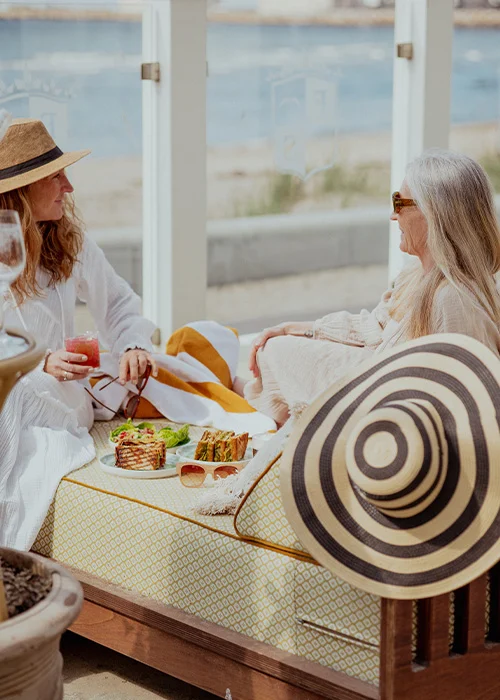 FSB – Spring Fling – Kellys Två kvinnor njuter av lunch med havsutsikt på Falkenberg Strandbads terrass under vårsolen
