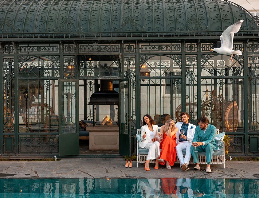 Eleganta gäster njuter av champagne vid poolkanten framför Strandbaden Falkenbergs historiska orangeri