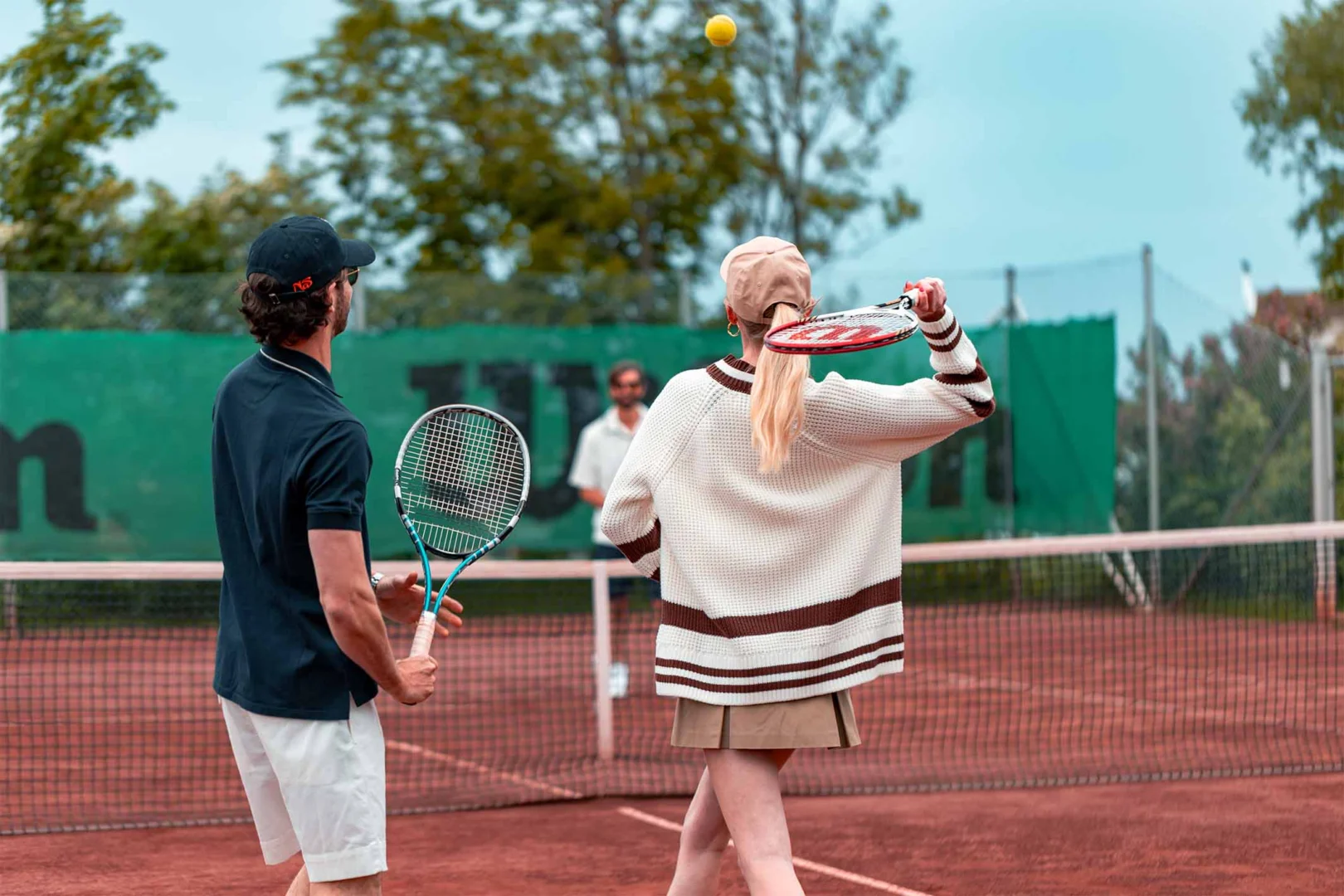 Tennislektion på röd grusbana vid Falkenberg Strandbad med instruktör och spelare i solsken