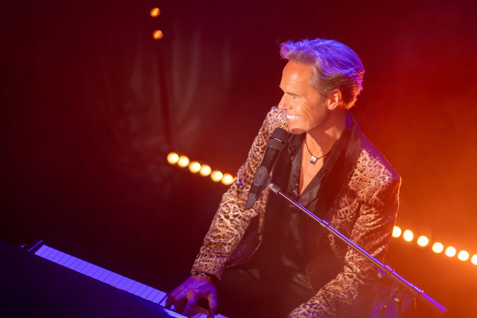 Underhållare i glittrig kavaj spelar piano och sjunger på scen med stämningsfull belysning