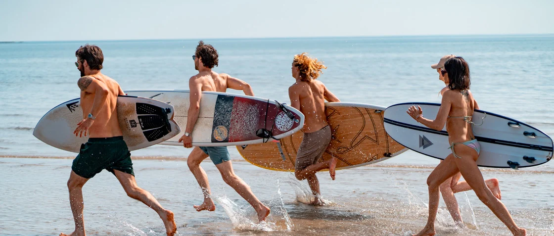 FSB-Aktiviteter-konferens-Vågsurfingkurs Fyra vänner springer med surfbrädor längs stranden vid Falkenberg Strandbad efter vågsurfingkurs