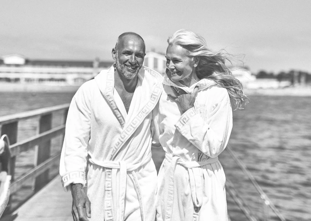 strandbaden-bryggan-havet-par Par i vita badrockar skrattar tillsammans på bryggan vid Falkenberg Strandbad efter avkopplande spabehandling